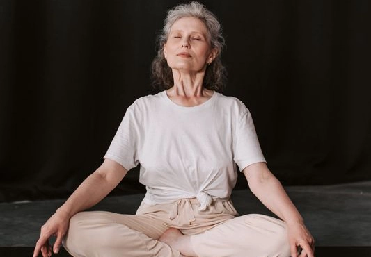 Eine Frau macht eine Atemübung und sitzt im Schneidersitz